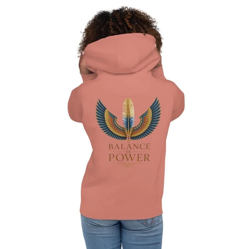 Person seen from behind wearing a salmon hoodie with a winged feather graphic and “BALANCE IS POWER” text.